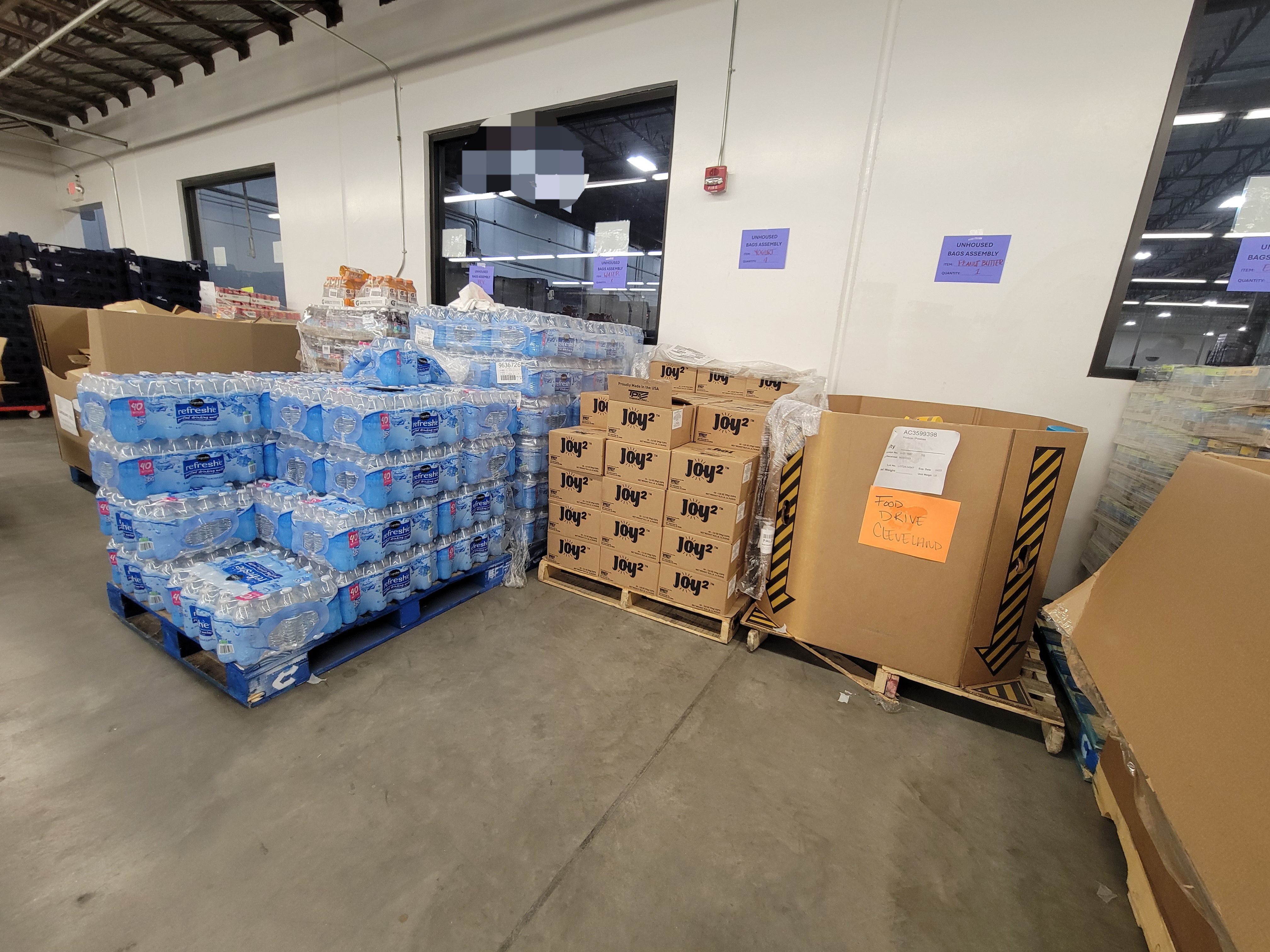Warehouse build area with alot of containers, pallet jack, two shopping carts, shelves and mop.